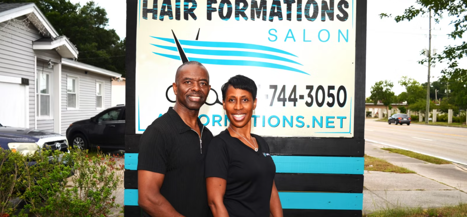 Aaron Gipson, a Marine Corps veteran, and his wife, LaVonia, co‑owners of Hair Formations Salon in Jacksonville, FL, outside their business.