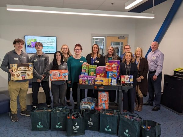 Students and credit union staff stand behind tables of donated food items collected for a local community food pantry.