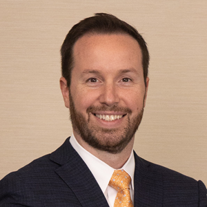 Headshot of Ben Lemoine, CFO of Suncoast Credit Union, wearing a navy suit, white shirt, and orange tie against a neutral background.