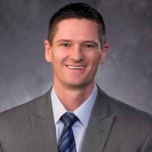 Headshot of Matt Kershaw, CEO of Create Credit Union, smiling in a gray suit, light blue shirt, and blue striped tie against a gray studio background.